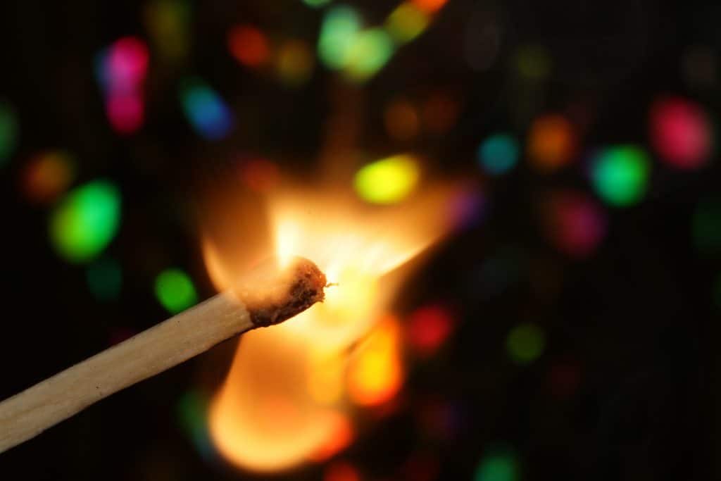 Photo of a match stick lighted up with different colors in the background